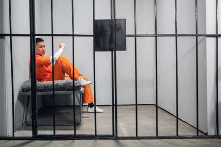 Solitary cell with a criminal in an orange robe in an asian prison. Copy space. Sad emotions of a young guyの写真素材