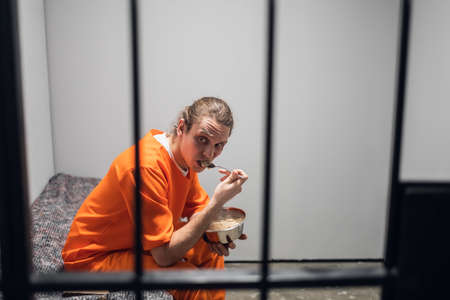 Dinner in a prison cell. A prisoner eats tasteless food from an iron bowl under guard behind bars