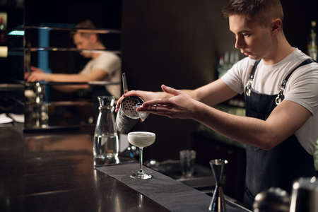 a young bartender makes a milk cocktail with a shaker on the bar.