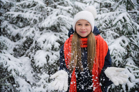 A playful teenage girl with a beautiful smile throws snow flakes and rejoices at the onset of the...