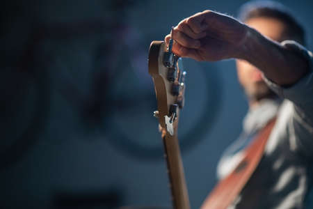the bassist adjusts the electric bass guitar, in the foreground of the pegs and fretboard, close-upの写真素材