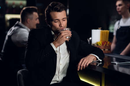 a beautiful man poses for a photo at the bar of a restaurant with a cocktail in his hands, portrait.の写真素材