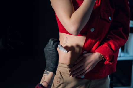 Cute brunette came to the tattoo parlor to get a tattoo, her master puts a sketch on the body.の写真素材