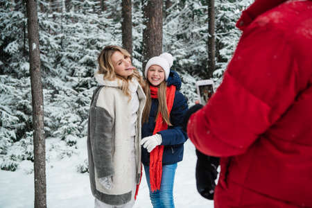 During a walk through the winter forest, a father takes photos of a mother and daughter on a...