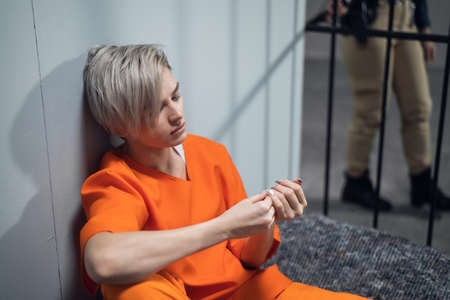 Sad girl criminal thinks about his fate, sitting on a prison bed.の写真素材
