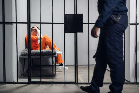 A prison guard makes a tour of the cells in a high-security prison. The cells are occupied by criminals in red robesの写真素材