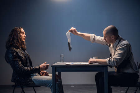 A bald strong police investigator presents evidence to the accused in the case of illegal distribution and storage of weapons in the police stationの写真素材