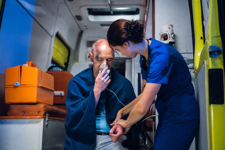 A female paramedic providing first aid to an injured man resqued from the fire, checking his pulse.の写真素材