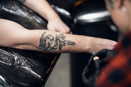 A tattoo artist with short hair and piercings is preparing to get a tattoo on a mans arm in a tattoo parlor.の写真素材