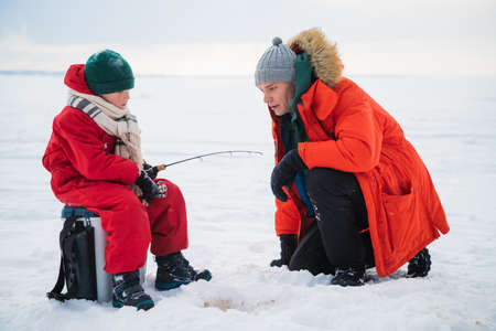 A young father teaches his son the basics of winter fishing on the ice of a lake in the village.の写真素材