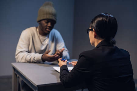 A lawyer girl with glasses and a young black guy communicate in the interrogation room about the grounds for his detention.の写真素材