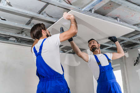 Adjusters in blue overalls stand on a ladder and make a ceiling