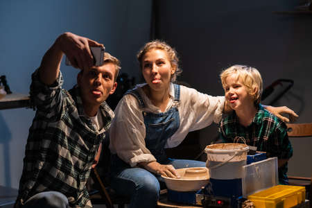 family dad, mom and son make faces for selfies in a pottery workshop