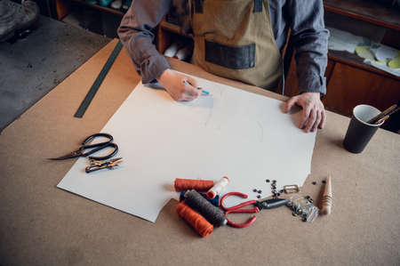 In a family shoe shop a young apprentice works with paper to create a pattern for shoes.
