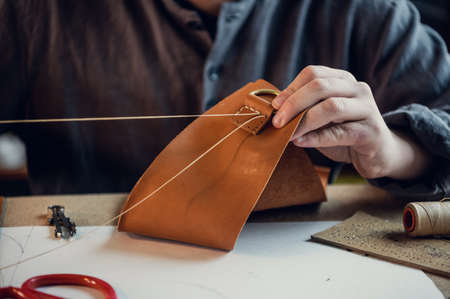 Close-up photo the hands of a skilled shoemaker make a bag from a piece of genuine leather.の写真素材