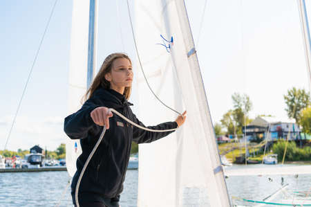 Young athletic girl in sports clothes on a yacht in the dock is ready for a sailing regatta