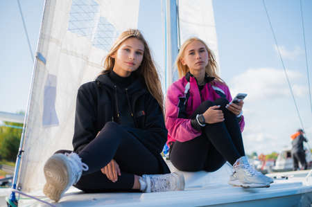 Two beautiful young female athletes during the regatta check the course using the navigator app in their smartphone, sitting on board the yachtの写真素材