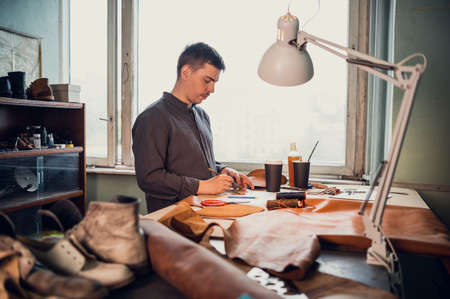 A young old-school shoemaker fulfills an order to make an exclusive leather product. Portrait in the...