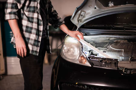 Amateur mechanic in the garage performs visual diagnostics of the engine injector under the hood of the car using a lampの写真素材