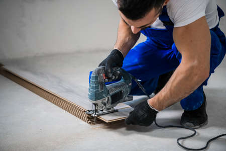 Woodworker in blue work clothes sawing laminate boards with an electric saw