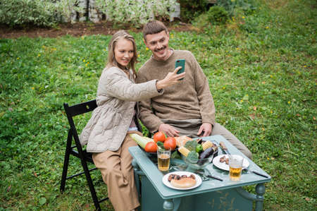 Modern husband and wife have fun taking an emotional selfie together during a picnic. Sitting at a...