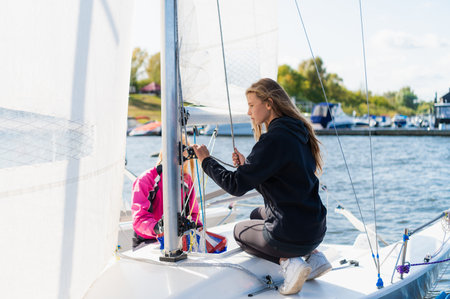 On the pier, two pretty girls pull sails on a boat to participate in a sailing competition.の写真素材
