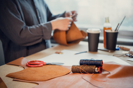 Close-up photo with the depth of field of the thread coils in the foreground. A shoemaker works at a...