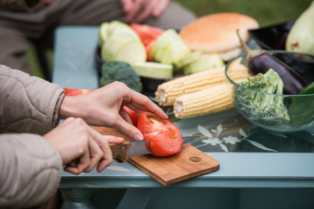 Joyful efforts to prepare for a family holiday in the yard. Hands of a man and a woman preparing vegetables for grilling for a picnic. Without a faceの写真素材