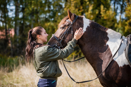 The owner of a horse strokes and caresses her horse on an autumn day on the farm.
