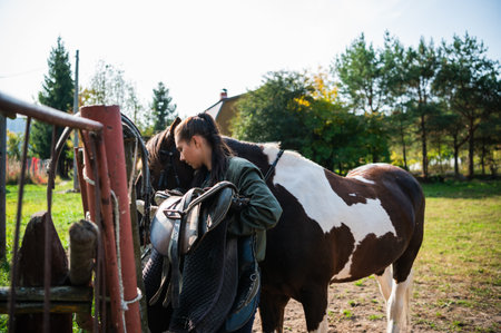 After a ride, the jockey unsaddles the horse next to the fence at the ranch.の写真素材