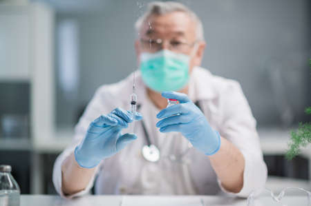 The coronavirus vaccine and the vaccination syringe are in the hands of an experienced medical professional. The doctors desk in the clinics medical office.の写真素材