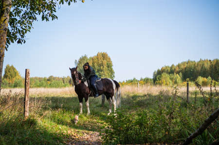 A pretty girl came to the country equestrian club and rides a horse through the fields in the fall.の写真素材