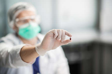 Close-up: in the laboratory, a young specialist with glasses and mask holds a capsule with a drug in his hands.の写真素材