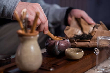 A man is passionate about the process of brewing fragrant black PU-erh tea. Throws the tea leaves into a special teapot on gongfu trayの写真素材
