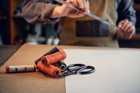 A young shoemaker makes a drawing for a pattern for leather shoes on a table in his workshop.の写真素材