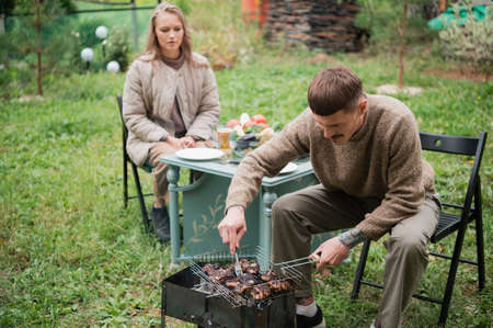 The husband, the head of the family, prepares steak and barbecue for his wife during an outdoor dinner. On the lawn in the courtyard of a country houseの写真素材
