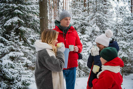 Dad and mom went out with the children to enjoy the winter nature in a snow-covered forest with firs and pines. Delicious warming tea in a vacuum flaskの写真素材