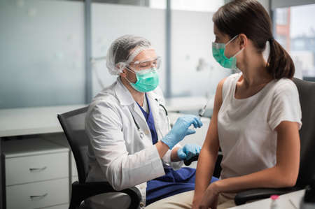 An experienced doctor in a mask does the vaccination in his office in a private clinic.の写真素材