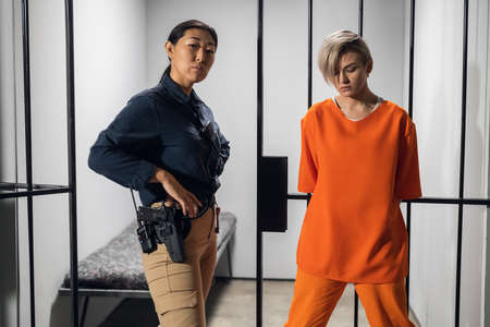 Shooting a movie about a womens prison. Backstage. Asian warden and a criminal girl in a yellow robe on the background of a prison cellの写真素材