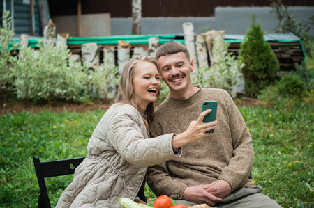 Selfies on a smartphone for social networks are made by a girl and a guy, sitting at a picnic table...