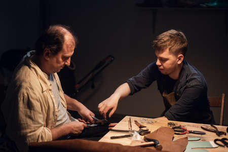 a respectable elderly shoemaker conducts a master class for a young boy on making shoes by hand in a special workshopの写真素材