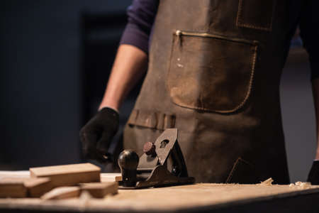 a young carpenter in an apron works in a carpenters shop, making wood productsの写真素材