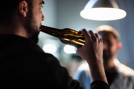 friends guys gathered at a bachelor party in the garage, drinking beer from dark bottles at a partyの写真素材