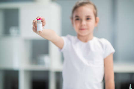 Close-up of a vaccine bottle held by a little girl against a white shelf.の写真素材
