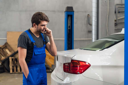 Mechanic looking at a car and talking on the phoneの写真素材