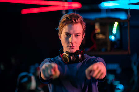 A cool gamer in a headset around his neck shows his hands to the camera and invites you to join a computer gameの写真素材