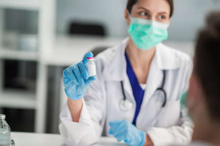 A young medical woman holds a bottle of vaccine in her hands and shows itの写真素材