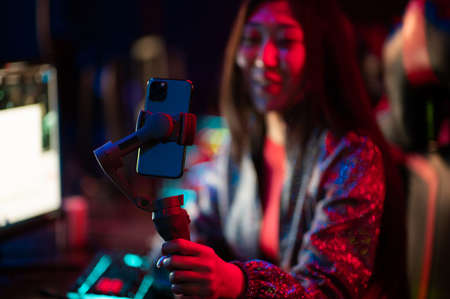 A young beautiful asian girl is broadcasting online on a smartphone with the help of a three-axis stabilizer. Female gamer at the esports tournament.の写真素材