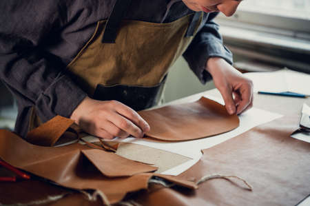 A talented young guy helps his father in the family business, cuts out blanks for shoes from leatherの写真素材