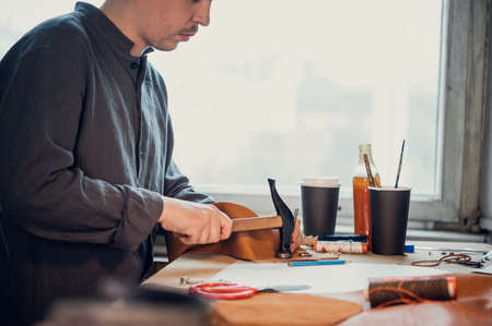 A young shoemaker using a hammer knocks down rivets on a leather product made with his own handsの写真素材